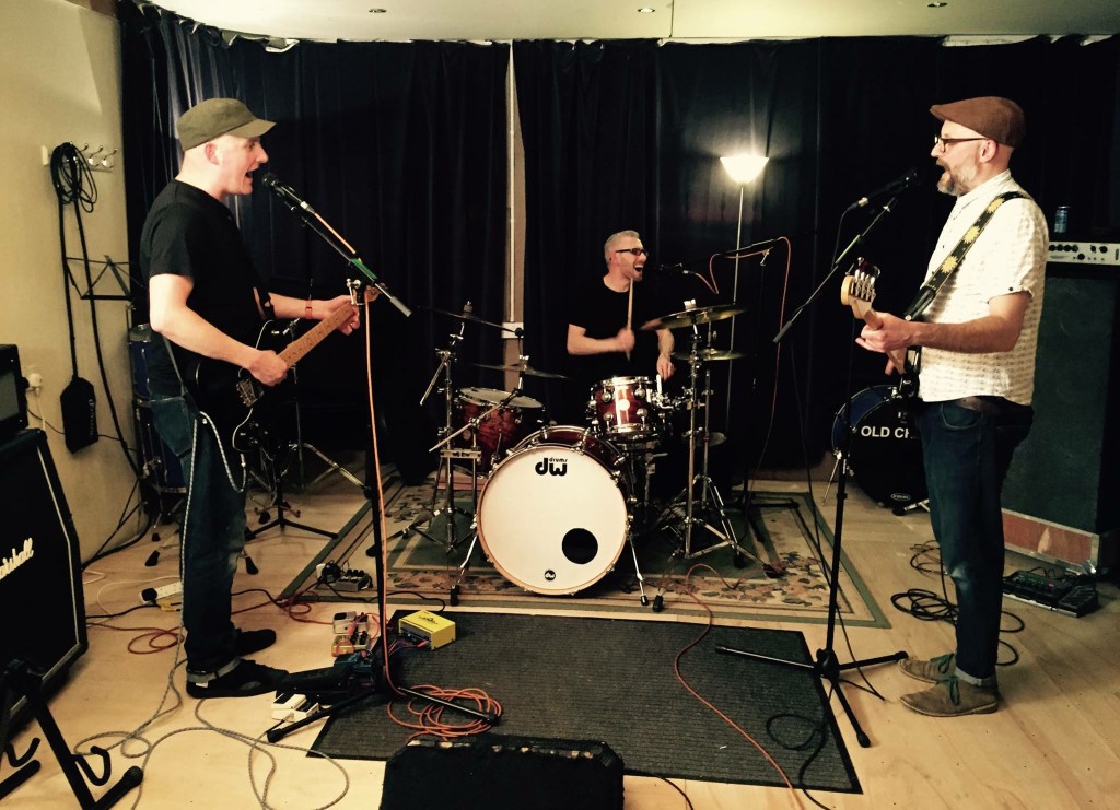 Image of a drummer, bassist and guitarist in a studio setting