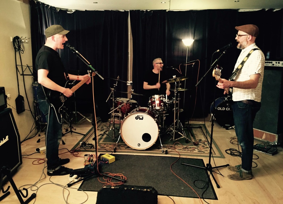 Image of a drummer, bassist and guitarist in a studio setting